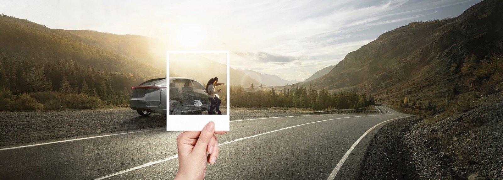 Two people standing beside an electric vehicle parked on a roadside in the mountains