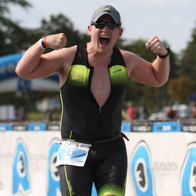 Triathlete Luke Laidlaw celebrates at the finish line with arms raised in triumph.