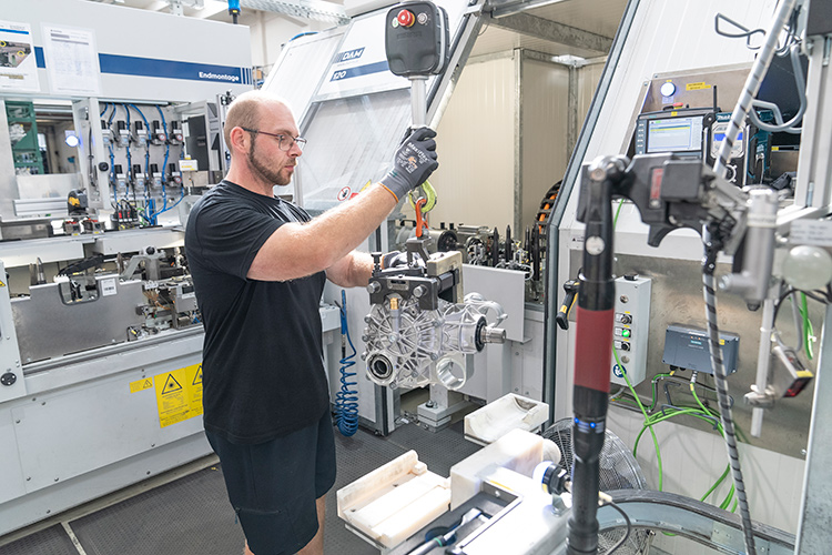 Factory worker using machinery to assemble a metal automotive part.