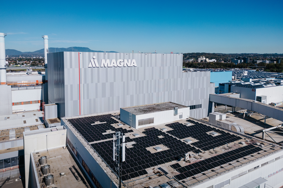 Magna factory building with rooftop solar panels and cityscape in the background